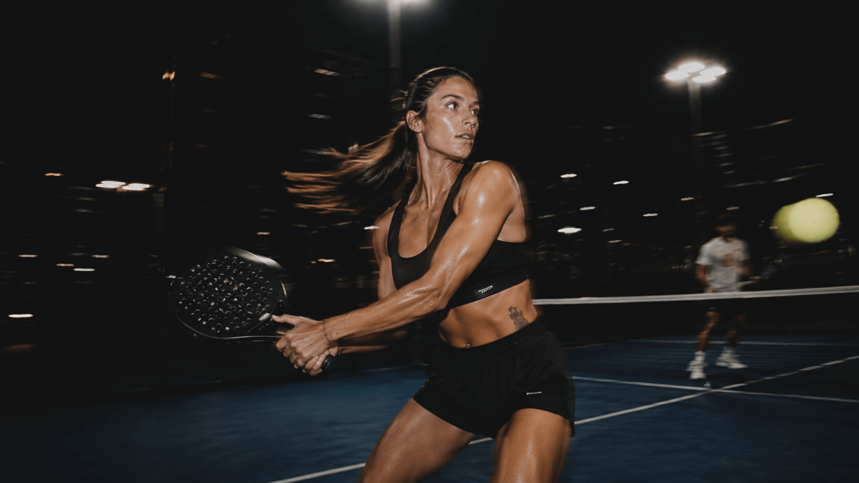 Padel player striking a two-handed backhand on a floodlit court at night